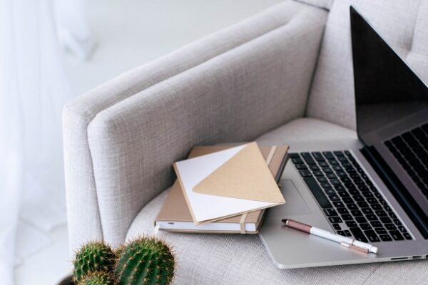 Decorative image of couch and a little table with a cactus, a notebook, and a laptop - 9 Signs It's Time to Outsource in Your Crafting Business