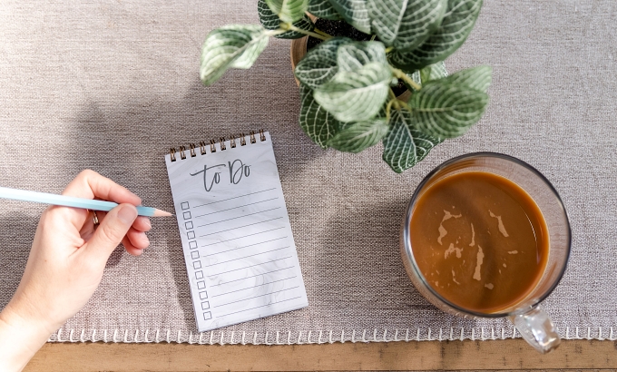 Flatlay with to-do list, hand holding a pencil, little plant, and cup of coffee - How to blog consistently for your author business