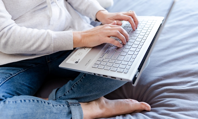 Woman sitting on her bed, typing on her laptop - How to blog consistently for your author business